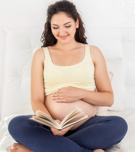 Cheerful young pregnant woman is resting in bedroom